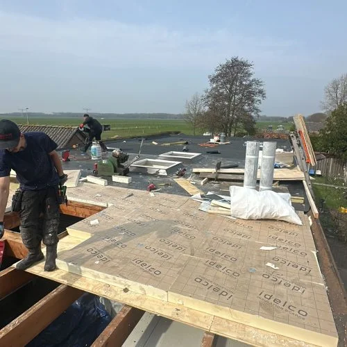 Platdak renovatie in Woerden met nieuw dakbeschot, 80 mm PIR isolatie, bitumen dakbedekking en vernieuwde dakkoepels.