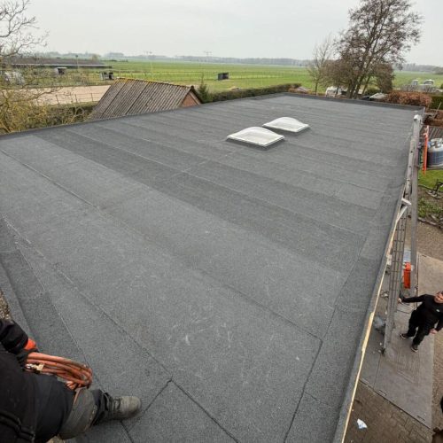 Platdak renovatie in Woerden met nieuw dakbeschot, 80 mm PIR isolatie, bitumen dakbedekking en vernieuwde dakkoepels.
