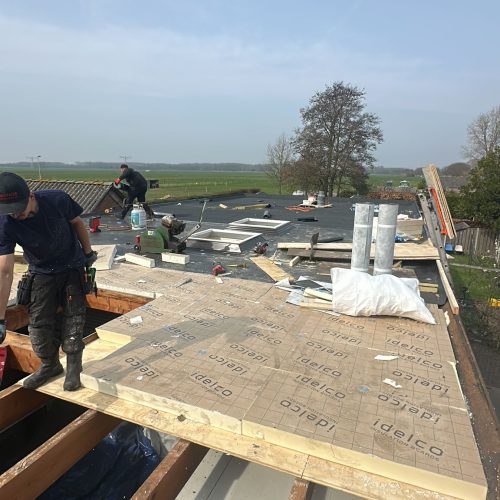 Platdak renovatie in Woerden met nieuw dakbeschot, 80 mm PIR isolatie, bitumen dakbedekking en vernieuwde dakkoepels.